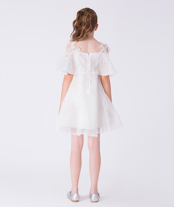 Back view of a sheer white girls dress featuring crystal flower shoulder straps and a light, flowing skirt for formal celebrations