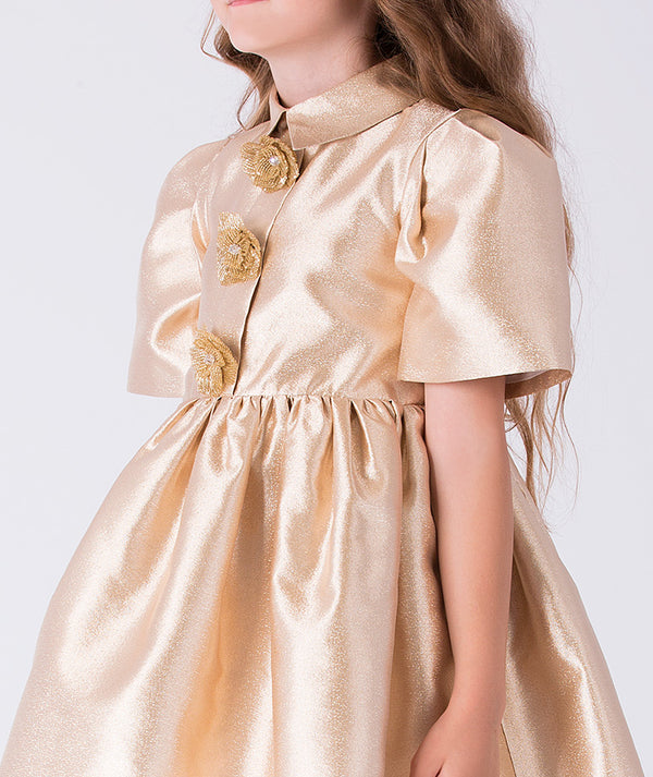 Close-up of metallic gold girls dress featuring decorative floral brooch appliqués and classic pointed collar detail.