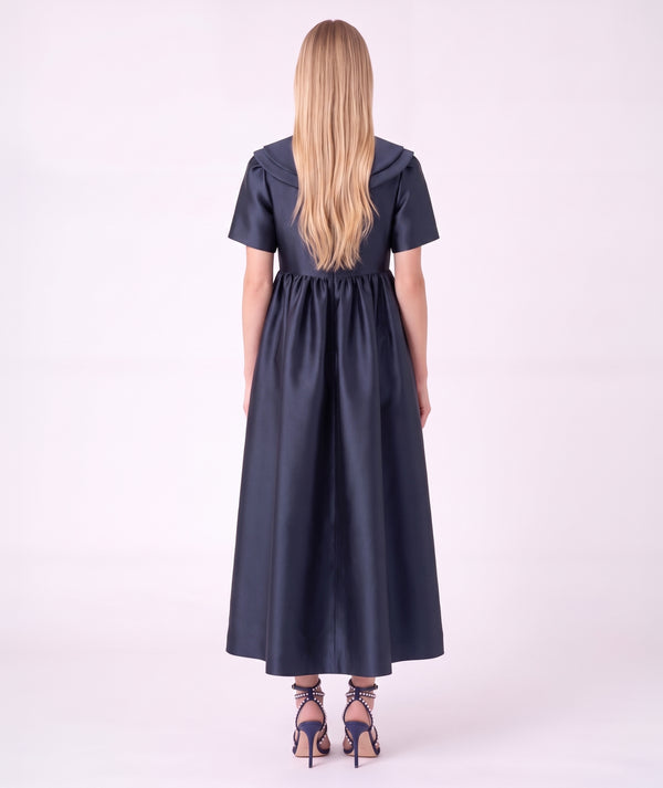 Back view of the Enchanting Brooch Women’s Dress from Mama Luma’s Suva Maia Collection, featuring a layered collar and full navy satin skirt.