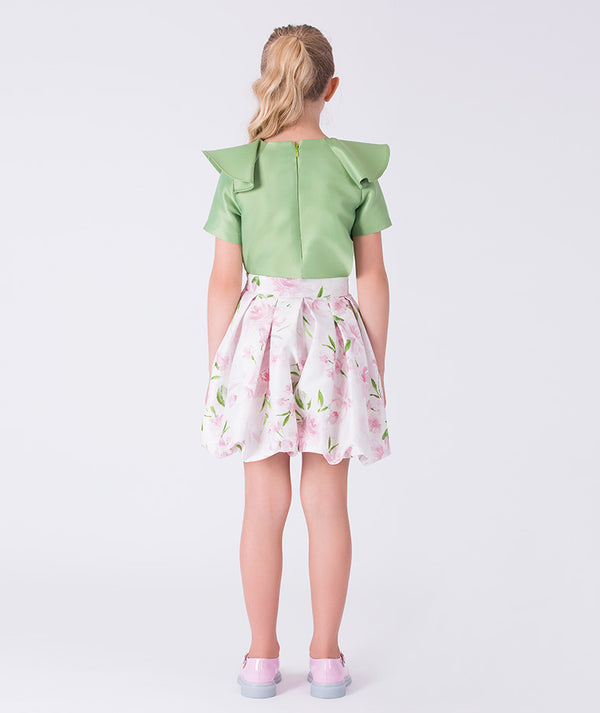 Back view of a two-piece girls outfit with sculptural shoulder detail and flared floral skirt, finished with a clean silhouette.