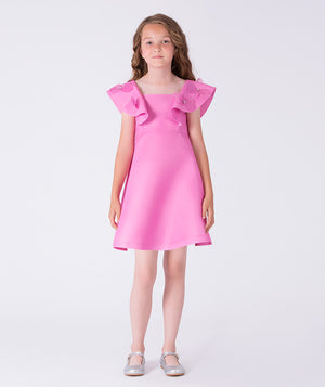 Luxury girls occasion dress in vibrant pink, worn by a 7-year-old girl, featuring sculptural ruffle shoulders, floral appliqués and a softly flared skirt for special events.