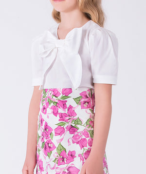 Close-up of front bow appliqué on a white top paired with a floral skirt in a girls two-piece occasion outfit.