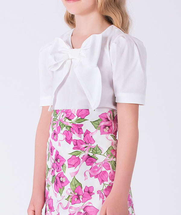 Close-up of front bow appliqué on a white top paired with a floral skirt in a girls two-piece occasion outfit.