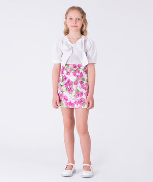 Front bow appliqué girls outfit worn by a 7-year-old girl, featuring a white top and floral skirt for special occasions.
