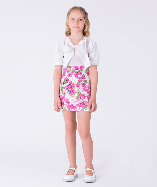 Front bow appliqué girls outfit worn by a 7-year-old girl, featuring a white top and floral skirt for special occasions.