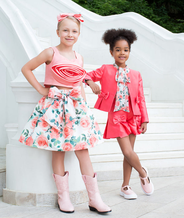 Girls coordinated coral and floral outfits featuring statement bows, skirts, and tailored jackets, styled for birthday celebrations, special occasions, and fashionable family events, available in sizes 3–12