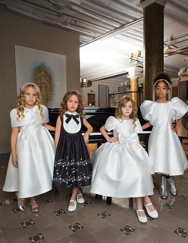 Girls model elegant white and black midi dresses with bows, puff sleeves and music-note embroidery