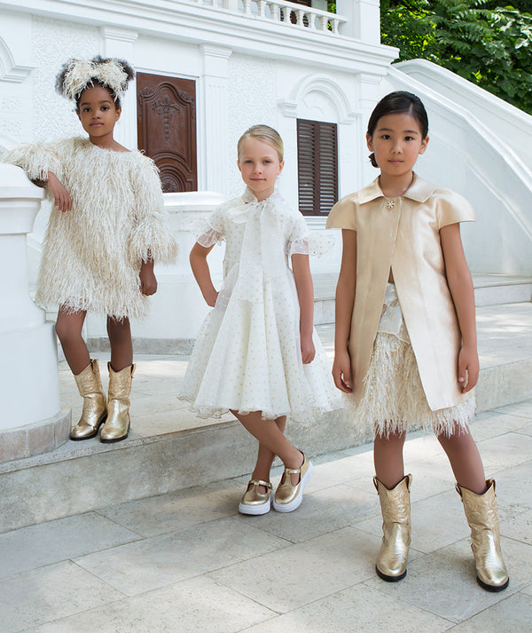 Girls ivory and champagne couture outfits with feather textures, sheer detailing, and elegant silhouettes, styled for weddings, holiday celebrations, family portraits, and formal occasions, available in sizes 3–12