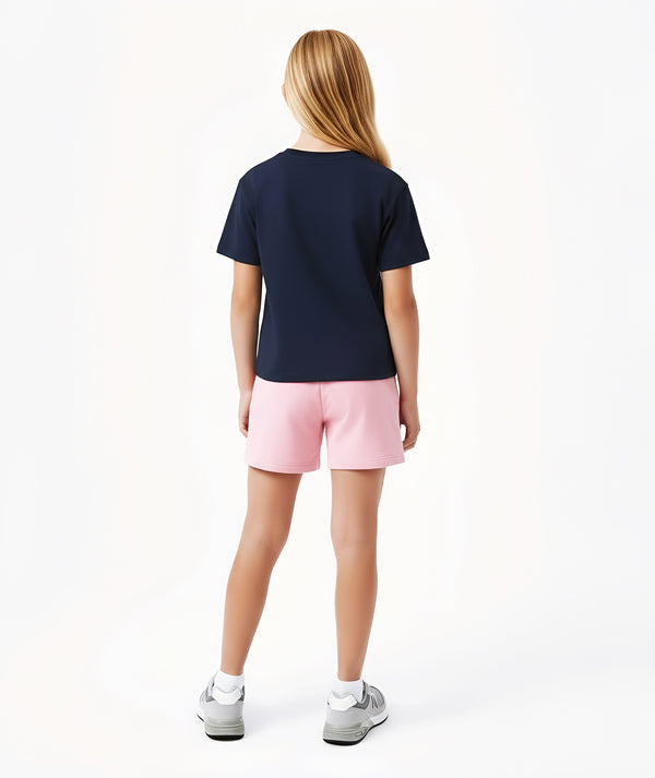 Girl seen from the back wearing a navy short sleeve t-shirt and pink shorts, styled for everyday athleisure, school days, and active play, available in sizes 3–14