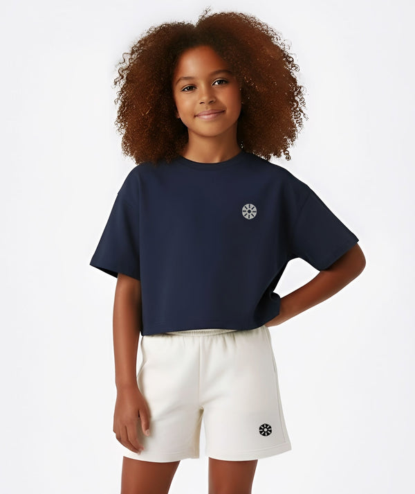 Front-facing lifestyle image of a girl wearing a navy short sleeve t-shirt with white shorts, styled for clean summer outfits, school-friendly comfort, and relaxed daily wear, available in sizes 3–14