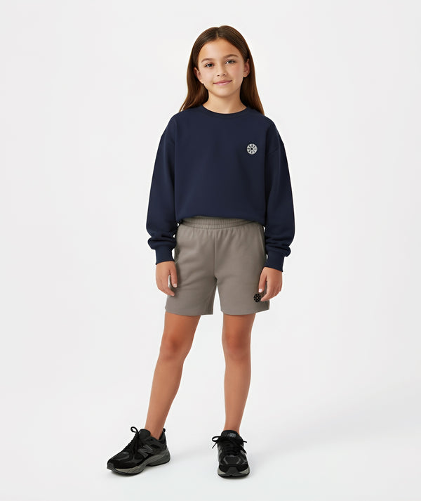 Girl wearing a navy sweatshirt and taupe shorts, styled for everyday athleisure, school days, and active play, available in sizes 3–14