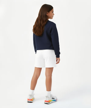 Three-quarter back lifestyle image of a girl wearing a navy sweatshirt with white shorts, styled for transitional weather outfits, casual school wear, and relaxed daily movement, available in sizes 3–14