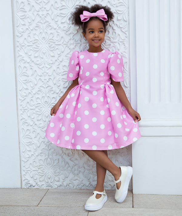 Girls pastel pink polka dot dress with puff sleeves and a softly structured skirt, styled for birthday parties, special celebrations, family photos, and joyful spring events, available in sizes 3–12