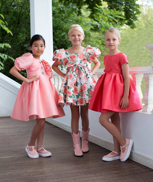 Girls elegant pink and coral dresses featuring floral prints, puff sleeves, and softly structured silhouettes, styled for birthday celebrations, weddings, family gatherings, and special spring occasions, available in sizes 3–12