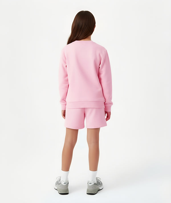 Girl seen from the back wearing a pink sweatshirt and matching shorts, styled for everyday athleisure, school days, and active play, available in sizes 3–14