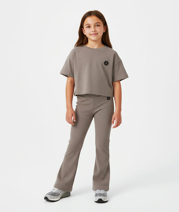Front-facing lifestyle image of a girl wearing a taupe short sleeve t-shirt with matching ribbed pants, styled for comfortable school days, casual movement, and everyday wear, available in sizes 3–14