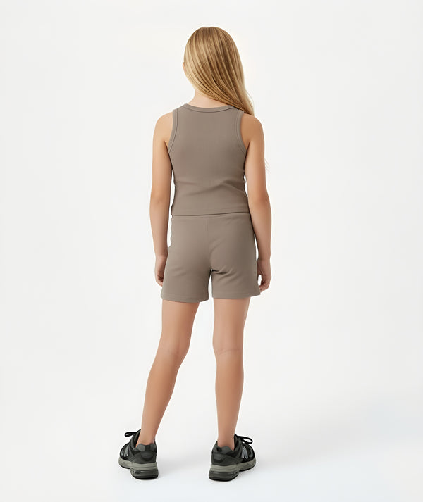 Back-facing lifestyle image of a girl wearing a taupe sleeveless tank top with matching shorts, styled for warm-weather play, casual movement, and everyday comfort, available in sizes 3–14
