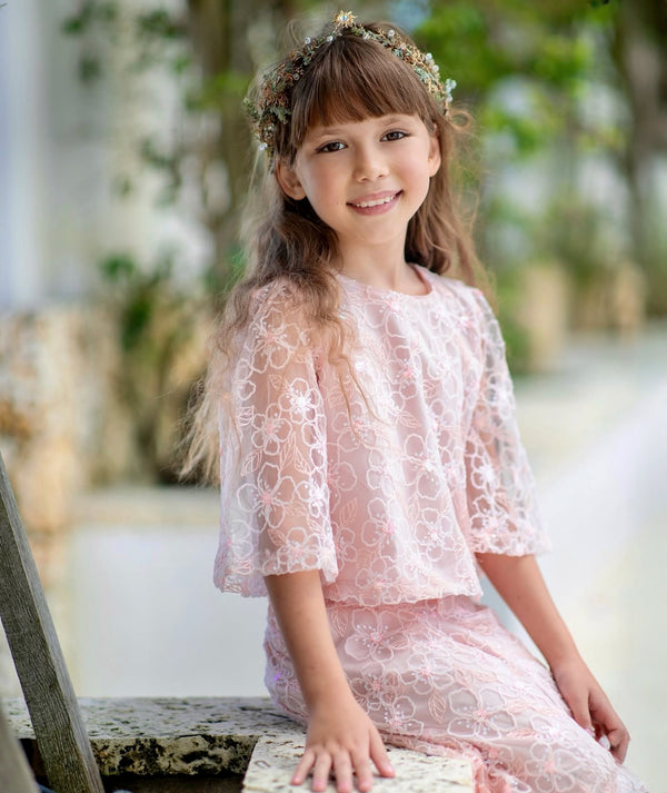 Girl in Mama Luma pastel pink lace outfit with floral embroidery and flared sleeves, styled with a flower crown — luxury girls’ wedding and flower girl dress