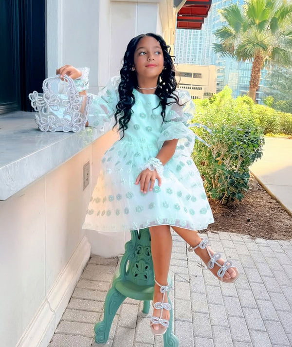Girl in Mama Luma mint green organza dress with puff sleeves and floral appliqués, styled with matching accessories — luxury girls’ wedding and party dress