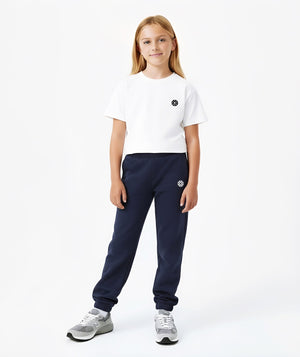 Front-facing lifestyle image of a girl wearing a white short sleeve t-shirt paired with navy jogger pants, styled for comfortable school routines, relaxed movement, and daily wear, available in sizes 3–14