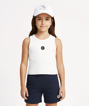 Front-facing lifestyle image of a girl wearing a white sleeveless tank top with navy shorts and a cap, styled for sporty outings, summer movement, and casual everyday wear, available in sizes 3–14