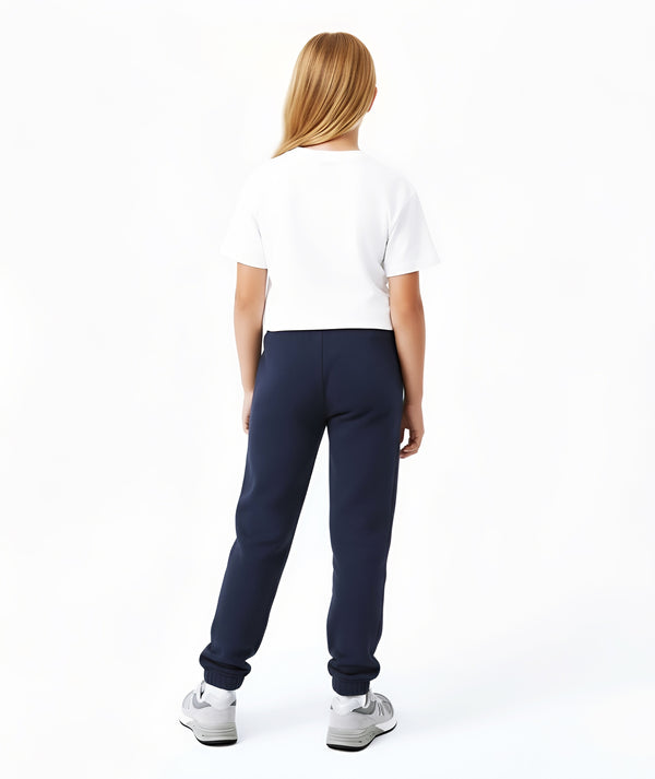 Back-facing lifestyle photo of a girl wearing a white short sleeve t-shirt with navy jogger pants, styled for relaxed school outfits, casual movement, and daily comfort, available in sizes 3–14