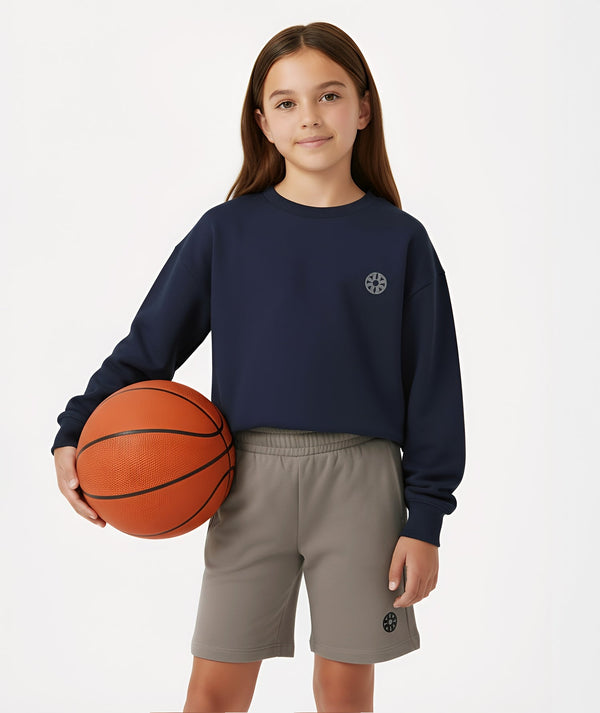 Girl wearing a navy sweatshirt and gray athletic shorts from GoldenCubs activewear collection, holding a basketball, standing confidently in a studio background.