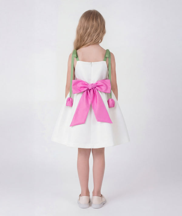 This elegant ivory girls dress features soft green shoulder straps adorned with 3D pink tulip details, creating a delicate yet statement look. Designed with a voluminous skirt and refined silhouette, it offers a premium special occasion style. The back view highlights its graceful structure and clean tailoring finish.