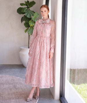 Woman wearing a blush pink floral jacquard dress with long sleeves and an oversized statement bow from the Hanae Collection