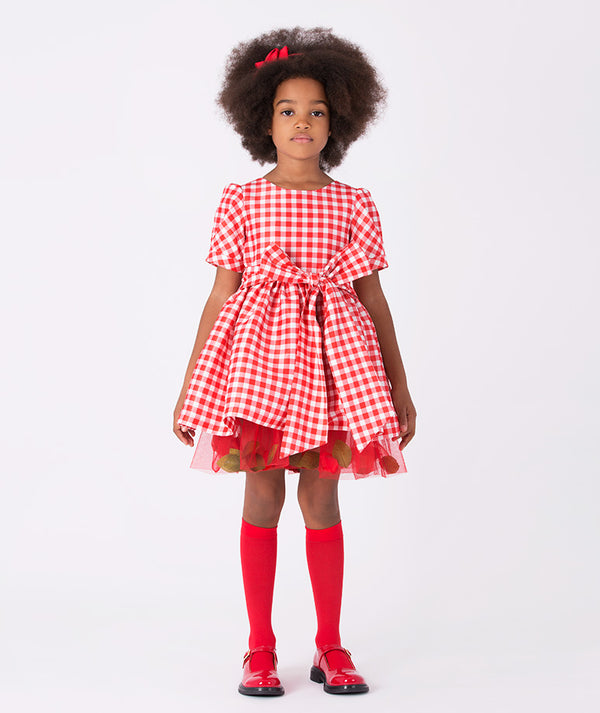 Girl wearing Mama Luma’s 3D Petals Plaid Dress in red-and-white checks with a bow and petal trim — perfect for Christmas parties, winter birthdays, and holiday photos. Available in girls’ sizes 3–12 Y.