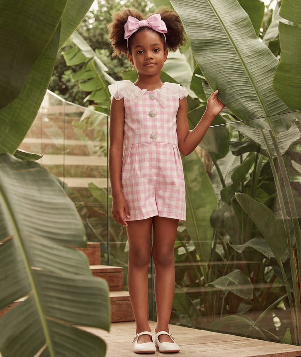 Young girl in a pink checkered dress standing among large green leaves.