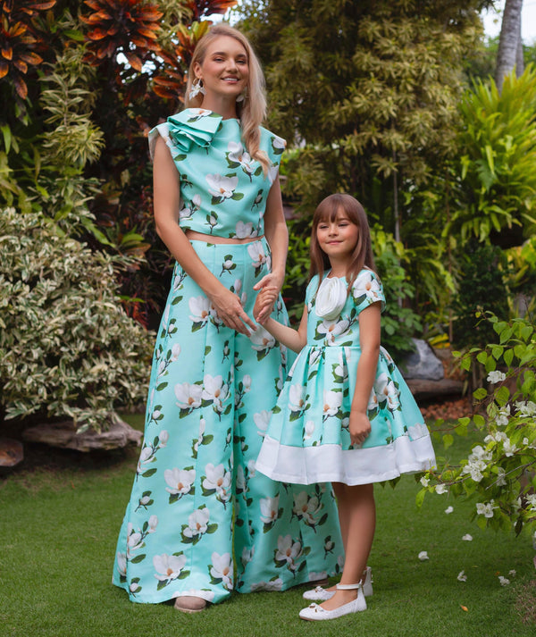 Woman and 6 years old girl in matching floral dresses standing outdoors with greenery around.