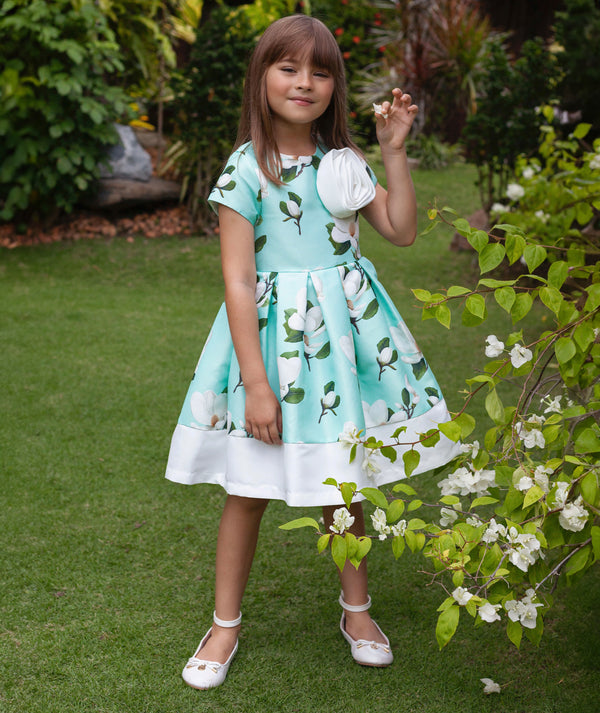 7 years old girl in a light blue dress with floral pattern standing in a garden.