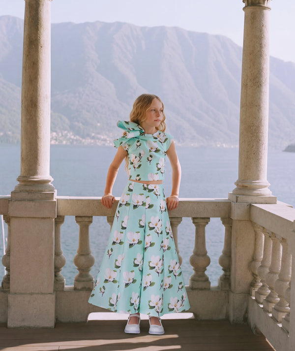 8 year old girl in a floral dress standing on a balcony with mountains in the background