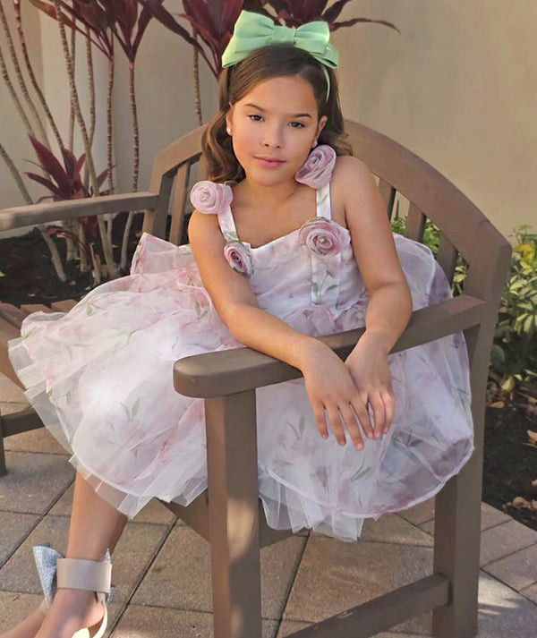 Young girl in a floral dress sitting on a wooden chair outdoors.