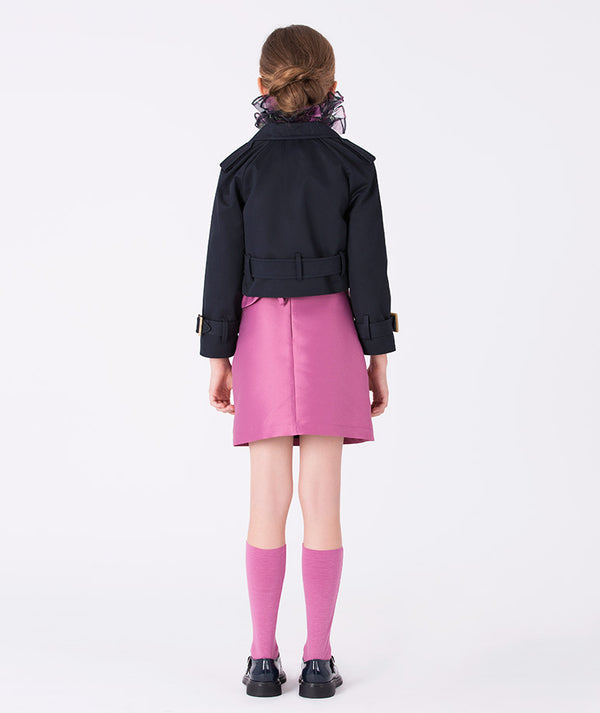 Girl seen from the back wearing a navy cropped jacket with belted waist and a fuchsia satin skirt by Mama Luma, styled with pink knee-high socks and black patent shoes. Perfect for weddings, birthdays, and elegant fall or winter celebrations. Available in girls’ sizes 3–12 years.