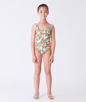 Girl wearing a Mama Luma orange floral one-piece swimsuit with ruffled shoulder straps and matching floral swim shoes. A vibrant summer outfit perfect for pool days, family vacations, and beach fun. Available in girls’ sizes 3–12 years.
