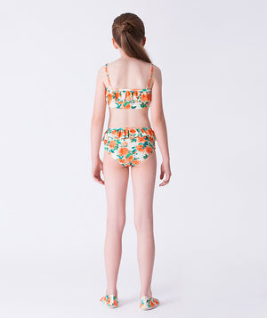 Girl seen from the back wearing a Mama Luma orange floral bikini with ruffle details and matching floral swim shoes. A bright, summery two-piece swimsuit perfect for beach days, vacations, and poolside fun. Available in girls’ sizes 3–12 years.