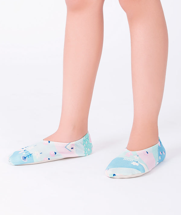 Girl wearing pastel blue printed swim shoes by Mama Luma. The slip-on design features an abstract beach pattern with light pink and mint tones. Perfect for beach days, poolside fun, and summer vacations.