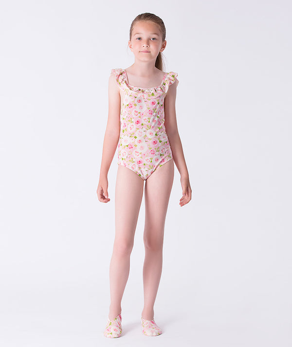 Girl wearing a Mama Luma pink floral one-piece swimsuit with ruffle shoulder straps and matching floral swim shoes. A sweet, summery look perfect for pool days, beach vacations, and resort wear. Available in girls’ sizes 3–12 years.