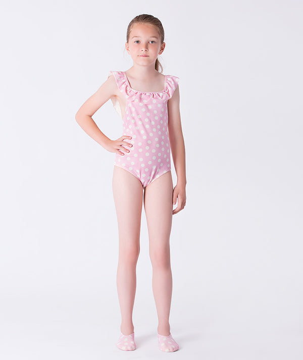 Girl wearing a Mama Luma pink polka-dot one-piece swimsuit with ruffled shoulder straps and matching polka-dot swim shoes. A playful and elegant summer look perfect for beach days, vacations, and poolside fun. Available in girls’ sizes 3–12 years.