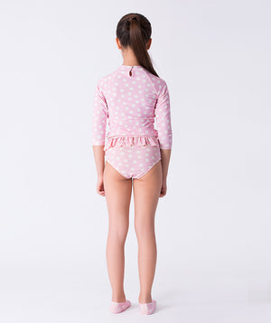 Girl seen from the back wearing a Mama Luma pink polka-dot long-sleeve rash guard swimsuit with ruffle waist and matching swim shoes. Perfect for pool days, beach vacations, and summer fun. Available in girls’ sizes 3–12 years.