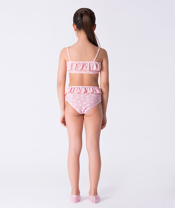 Girl seen from the back wearing a Mama Luma pink polka-dot bikini with ruffle details and matching swim shoes. A stylish two-piece swimsuit perfect for beach vacations, pool days, and summer adventures. Available in girls’ sizes 3–12 years.