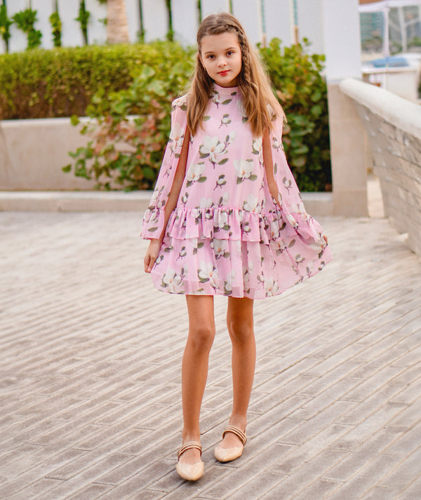 5 years old girl in a pink floral dress standing on a wooden boardwalk.