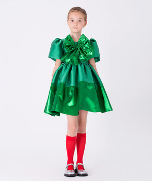 Girl wearing Mama Luma’s Shimmering Bow Dress in emerald green with puff sleeves and metallic bow — perfect for Christmas parties, family gatherings, and winter weddings. Available in girls’ sizes 3–12 Y.