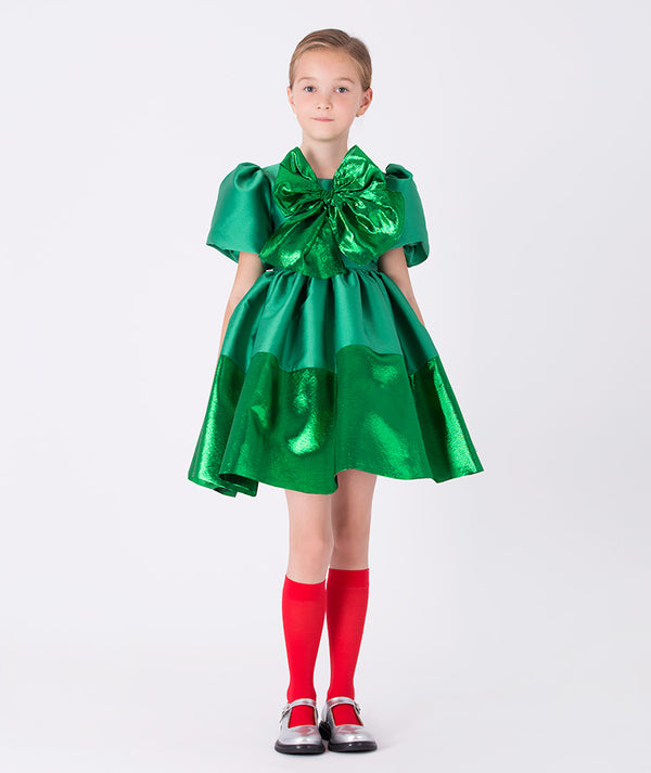 Girl wearing Mama Luma’s Shimmering Bow Dress in emerald green with puff sleeves and metallic bow — perfect for Christmas parties, family gatherings, and winter weddings. Available in girls’ sizes 3–12 Y.