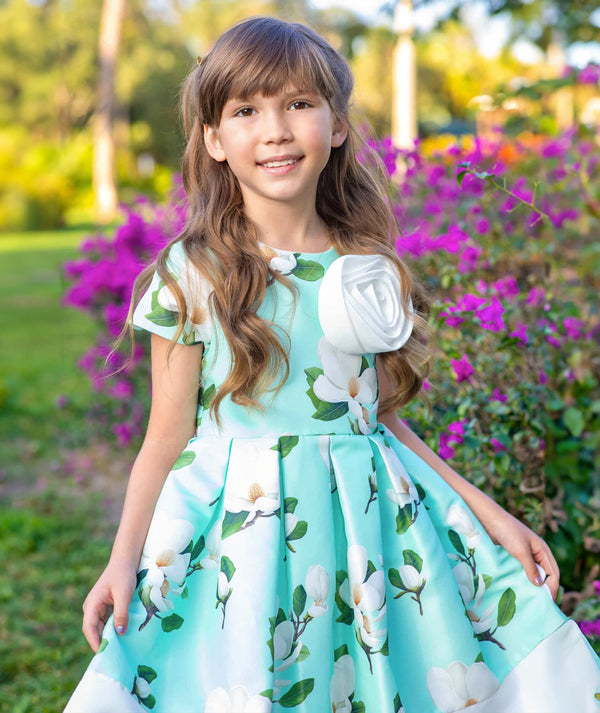 4 years old girl in a floral dress standing in a garden with flowers and greenery.