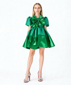 Front view of Mama Luma’s Women’s Green Shimmering Bow Dress, designed with metallic emerald satin, puff sleeves, and an oversized statement bow. Perfect for Christmas celebrations, New Year’s Eve, and winter gala events. Available in sizes XS–XL for elegant Mommy & Me matching.