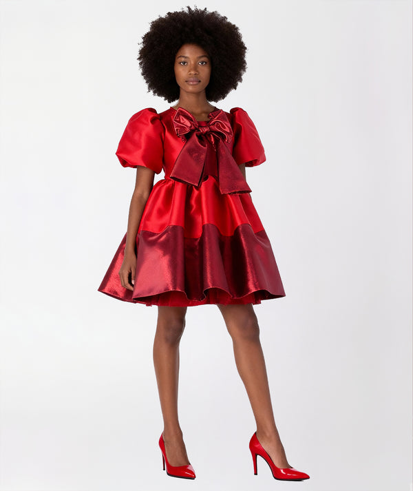 Front view of Mama Luma’s Women’s Shimmering Bow Dress in radiant red satin with metallic finish, featuring voluminous puff sleeves and a statement oversized bow. Perfect for Christmas celebrations, New Year’s Eve parties, and elegant holiday gatherings. Available in sizes XS–XL for Mommy & Me pairing.