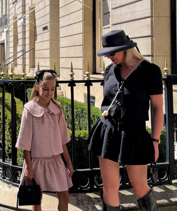 Mother and daughter in chic Mama Luma tweed outfits — girl in pastel pink jacket and skirt set with bow collar, mom in elegant black tweed set, perfect for parties and city occasions